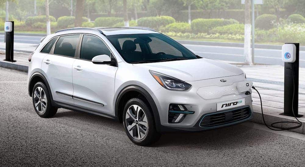 A white 2019 Kia Niro EV is shown at a charging station after visiting a used Kia dealer.